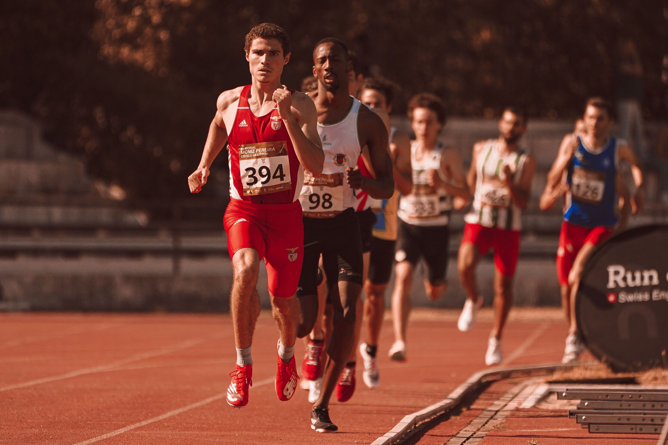 group of middle-distance runners racing on an outdoor athletics track on a sunny day
